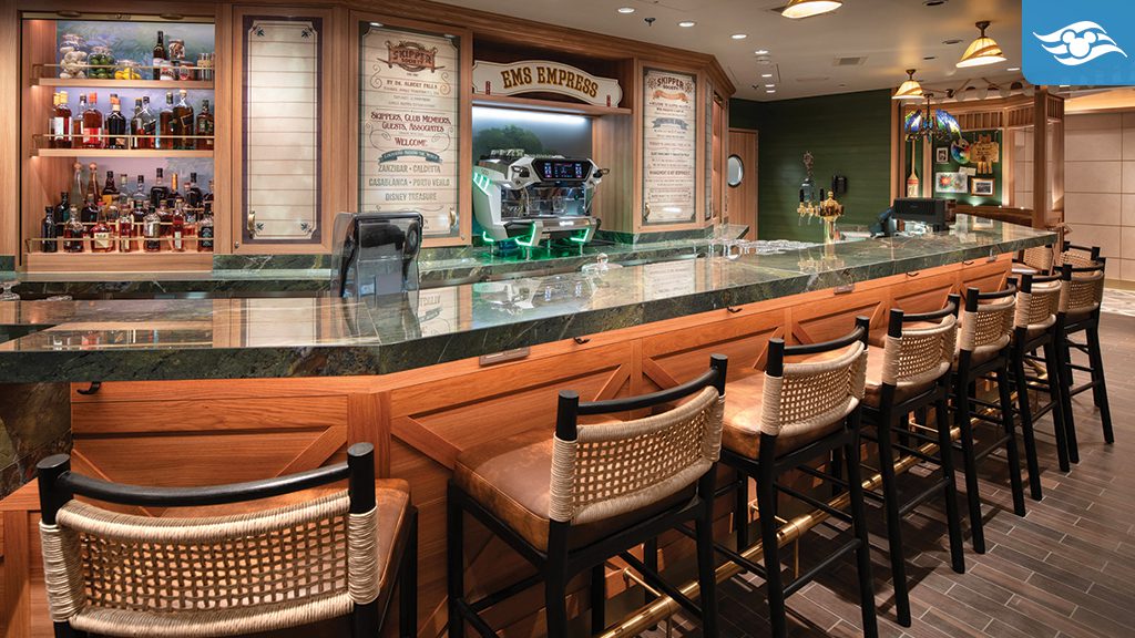 The Skipper Society lounge aboard the Disney Treasure, featuring a polished wooden bar with a green marble countertop, wicker-accented bar stools, tropical decor, parrot-shaped chandeliers, and a vintage travel-inspired ambiance.