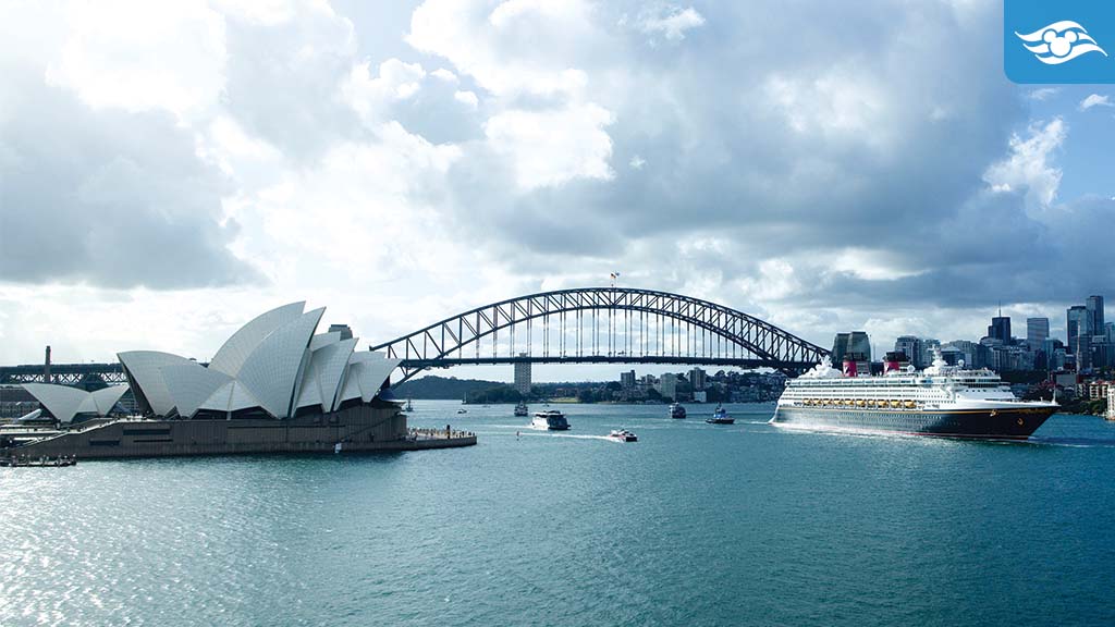 disney-cruise-line-wonder-australia A cruise ship sails past the Sydney Opera House and Sydney Harbour Bridge under a partly cloudy sky.