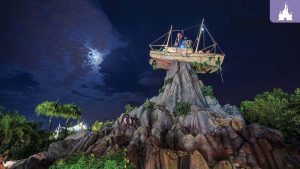 Moonlit night at Disney's Typhoon Lagoon with a shipwreck perched atop a rocky mountain, surrounded by lush tropical greenery.