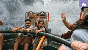 Two children laughing on a water ride at Disney World as a wave splashes over the boat.
