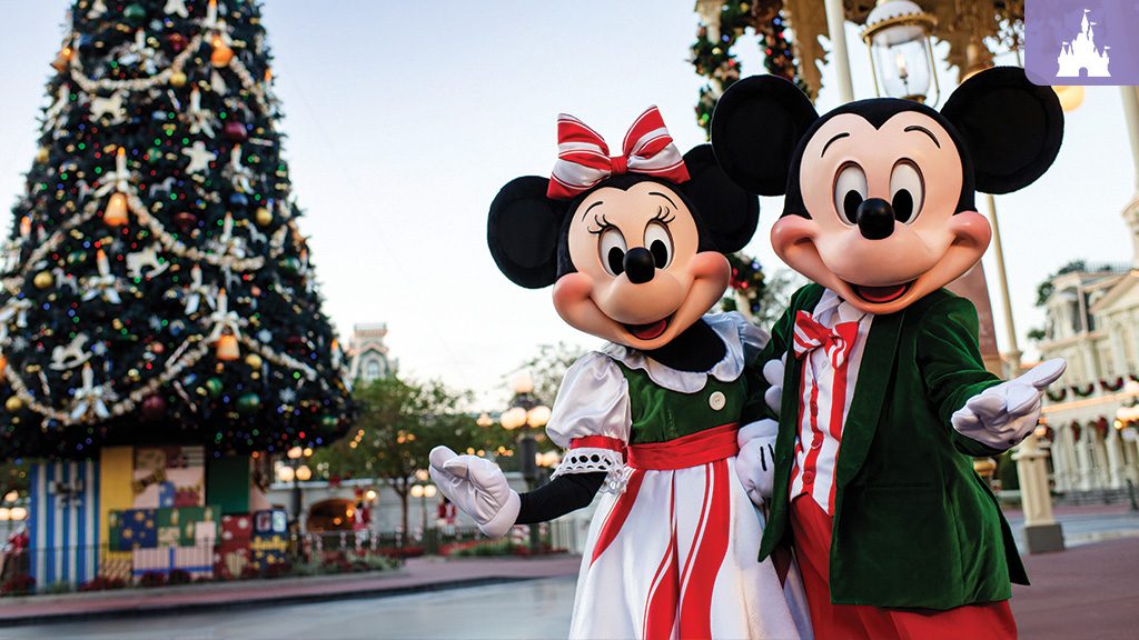 Mickey and Minnie Mouse dressed in festive holiday outfits standing in front of a large decorated Christmas tree at Walt Disney World’s Main Street, U.S.A., with ornaments, garlands, and gift boxes at the tree’s base.