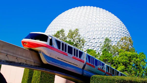 Disney Monorail glides past lush greenery with Spaceship Earth in the background at EPCOT in Walt Disney World.