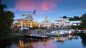 Disney’s Old Key West Resort at sunset, featuring waterfront docks, boats, and tropical architecture with glowing lights and a pink sky.