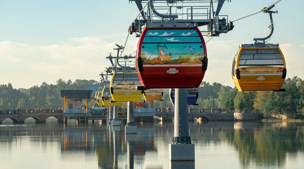 Colorful Disney Skyliner gondolas glide over water at Walt Disney World, offering scenic and efficient transportation between resorts and parks.