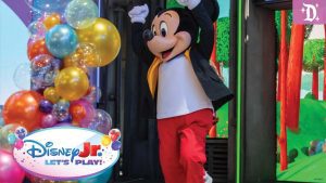 Mickey Mouse dancing on stage at Disney Jr. Let’s Play!, surrounded by colorful balloons and vibrant forest-themed decor.