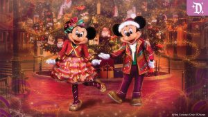 Mickey and Minnie Mouse in festive red and gold holiday outfits pose in front of a decorated Christmas tree at Disneyland.