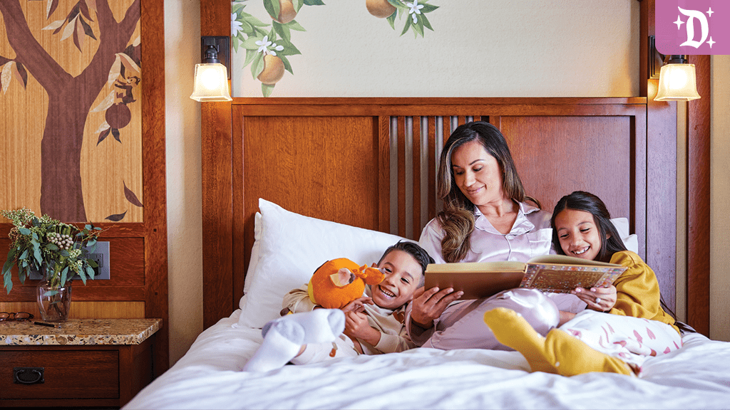 Mother reading a book to two children on a cozy bed at a Disneyland Resort hotel room decorated with nature-themed artwork.