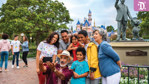 A multigenerational family poses for a selfie in front of the Sleeping Beauty Castle and the Partners statue at Disneyland, smiling and enjoying their visit.