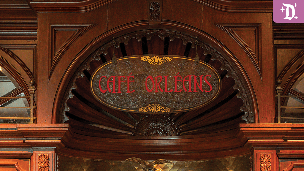 A wooden sign displaying "CAFÉ ORLEANS" in red text, set against an ornate background with intricate architectural details.