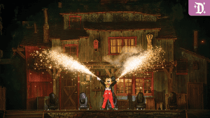 Mickey Mouse stands on stage in front of a rustic cabin, shooting sparks from handheld devices, surrounded by dramatic lighting.
