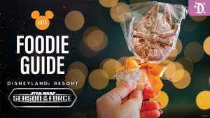 Hand holding a Millennium Falcon-shaped chocolate lollipop wrapped in clear plastic with a gold ribbon, promoting Disneyland Resort's Season of the Force Foodie Guide.