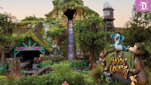 Entrance to Tiana’s Bayou Adventure in Disneyland's Bayou Country, featuring a rustic log flume ride with lush greenery, playful critter statues, and Tiana's Foods water tower in the background.