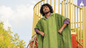 A person in a green poncho stands confidently on a playground structure, with trees and a cloudy sky in the background.