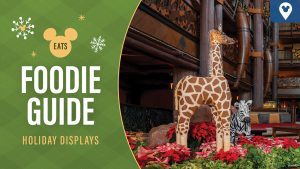 Gingerbread-themed holiday display at Disney's Animal Kingdom Lodge featuring a life-sized gingerbread giraffe and zebra surrounded by festive poinsettias and holiday decor in a rustic lodge setting.