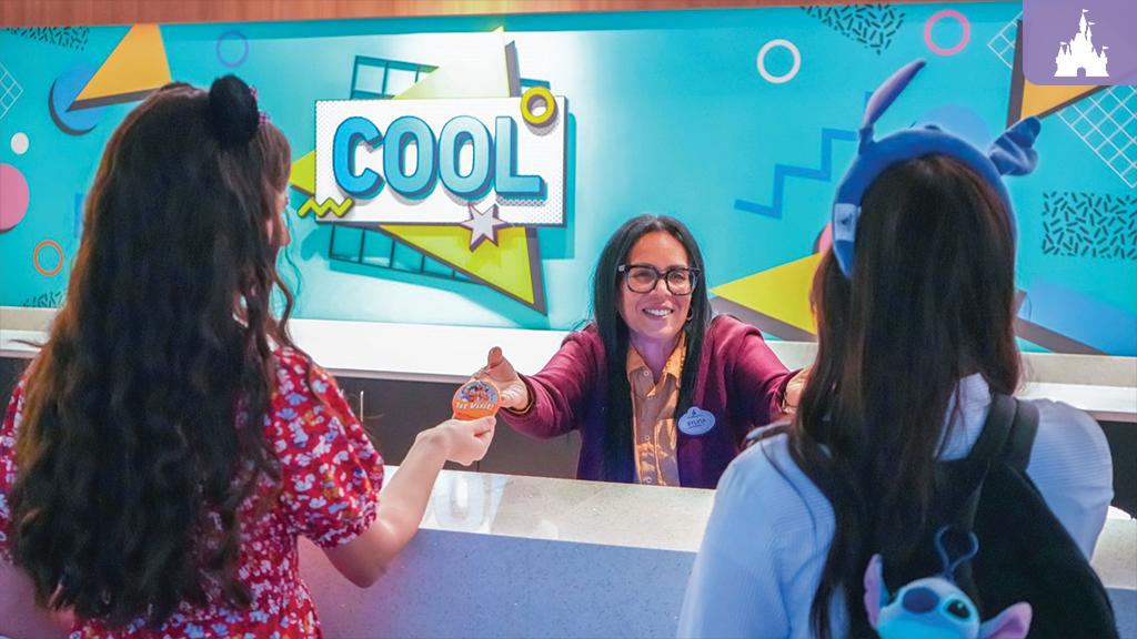 Disney cast member greeting guests at Pop Century Resort check-in desk with colorful retro “cool” wall design in background
