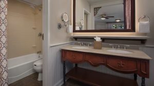 Elegant bathroom with a double vanity, framed mirror, and a shower-tub combo, designed with classic wooden accents.