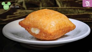A golden, crispy pastry on a white plate, featuring a small opening revealing a creamy filling inside.