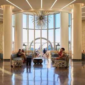 Guests relax in the modern lobby of Universal Helios Grand Hotel, with floor-to-ceiling windows and a large starburst chandelier.