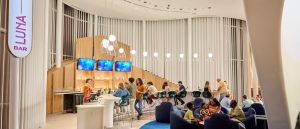 Guests enjoy drinks and conversation at the modern Luna Bar at Universal Terra Luna Resort, featuring a wood-accented bar and hanging lights.