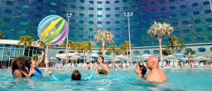 Families play with a beach ball in the pool at Universal Terra Luna Resort, with colorful hotel exterior and palm trees in the background.