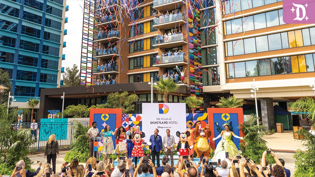 A cheerful gathering in front of a colorful hotel; costumed characters and a crowd celebrate a festive event outdoors.