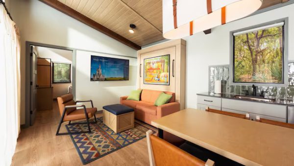 walt-disney-world-1-bedroom-cabin-fort-wilderness A cozy, modern living space features a sofa, chairs, dining table, and colorful artwork on the walls, with natural light from windows.