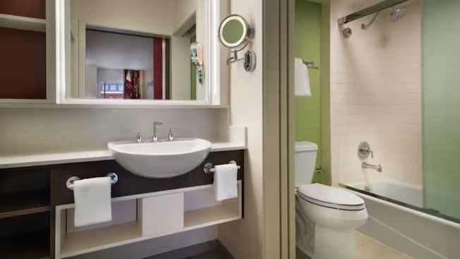 A modern bathroom featuring a white sink, mirror, toilet, and a bathtub with a shower curtain. Clean and well-lit design.