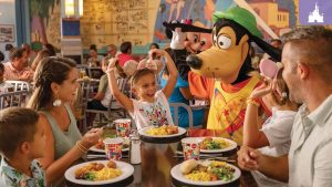 A family enjoying a character dining experience at Walt Disney World, with Goofy playfully interacting with a smiling child at the table, surrounded by colorful plates of food.