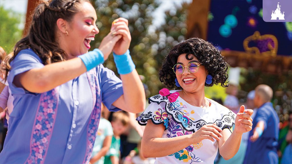 Two women joyfully dancing at a Disney celebration, one dressed as Mirabel from "Encanto," capturing the spirit of Hispanic and Latin American Heritage Month.