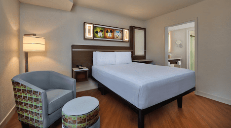 A cozy hotel room featuring a bed, a patterned chair, and a small table, with warm lighting and modern decor.