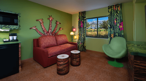 A colorful hotel room featuring a green wall, a red sofa, unique giraffe-themed decor, and large windows with vibrant curtains.