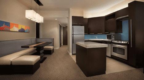 walt-disney-world-resort-bay-lake-tower-one-bedroom-villa-kitchen Modern kitchen featuring dark cabinetry, stainless steel appliances, a dining area with a built-in bench, and a colorful wall decoration.