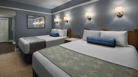 walt-disney-world-resort-beach-club-two-bedroom-villa-queen-room A hotel room featuring two beds with white linens, decorative blue pillows, and a star-patterned throw blanket against blue walls.