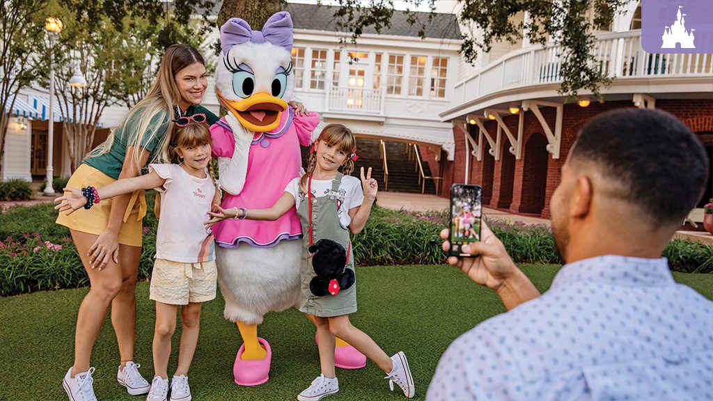 Family enjoying a magical moment with Daisy Duck at Disney World Resort, with a dad capturing the joyful scene on his phone for a lasting memory.