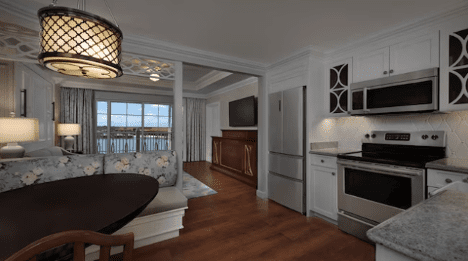 walt-disney-world-resort-grand-floridian-two-bedroom-villa-kitchen A bright, modern kitchen and dining area featuring wood floors, a round table, stainless steel appliances, and large windows with a scenic view.