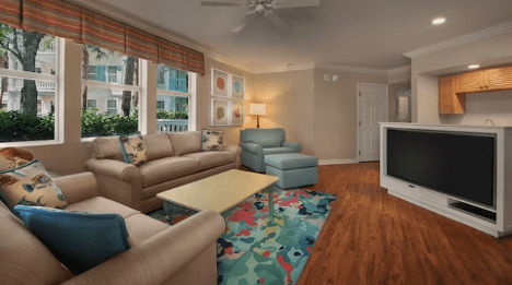 walt-disney-world-resort-old-key-west-one-bedroom-villa Bright living room featuring a spacious layout, beige sofas, colorful rug, and large windows letting in natural light. TV and kitchenette visible.