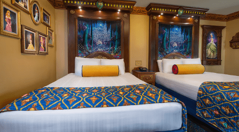 A cozy hotel room featuring two beds with decorative blue and gold bedding, framed pictures on the walls, and themed artwork behind the beds.