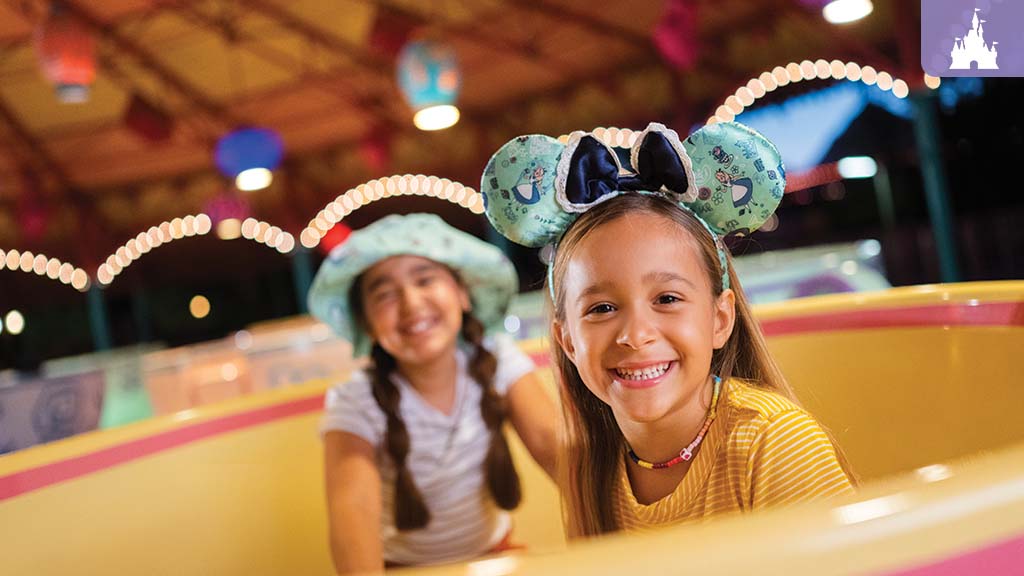 Two young girls smiling and enjoying a colorful teacup ride at Walt Disney World, wearing playful hats and Minnie Mouse ears.