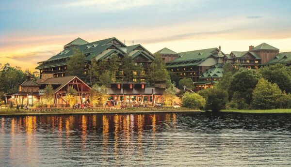A scenic view of a lodge by a tranquil lake at sunset, surrounded by trees and reflecting warm lights on the water.